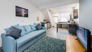 A modern living room with a blue sofa, a TV, and a kitchen in the background. - Infinity Apartments Harrow Road (Liverpool)