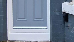 A grey door with a white frame, a small mailbox, and a doorbell on a grey brick wall. - Infinity Apartments Harrow Road (Liverpool)