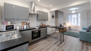 A modern kitchen with a central island, built-in oven, and stainless steel appliances. - Infinity Apartments Harrow Road (Liverpool)