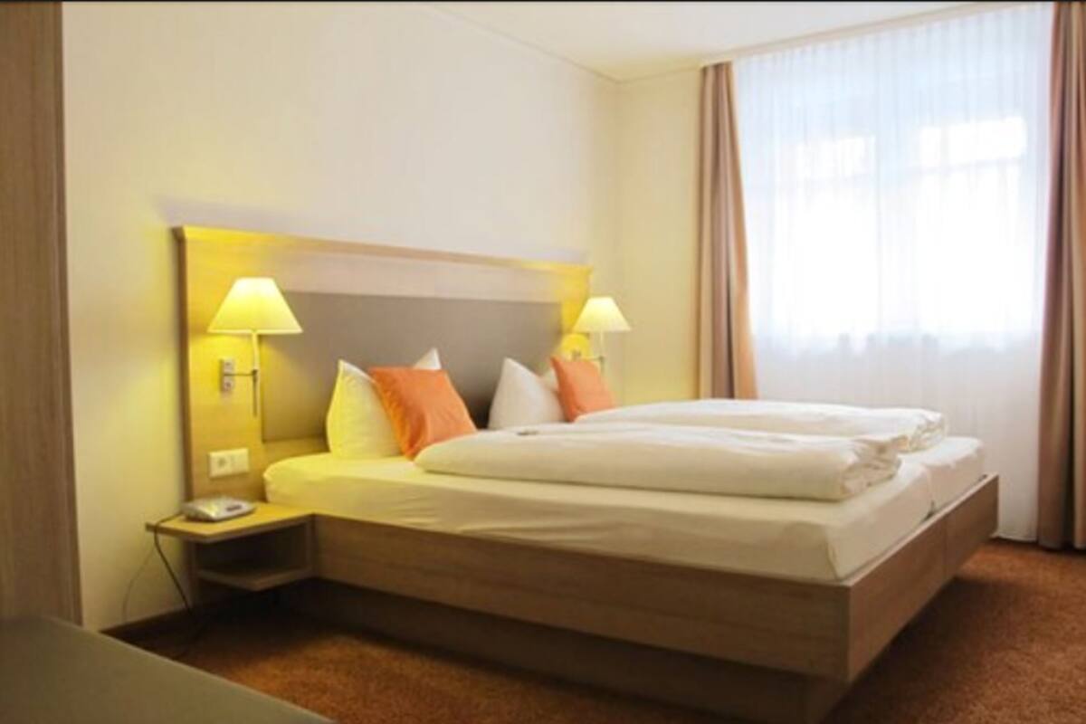 Een hotelkamer met een groot bed, twee bedlampen, een nachtkastje en een raam met gordijnen.