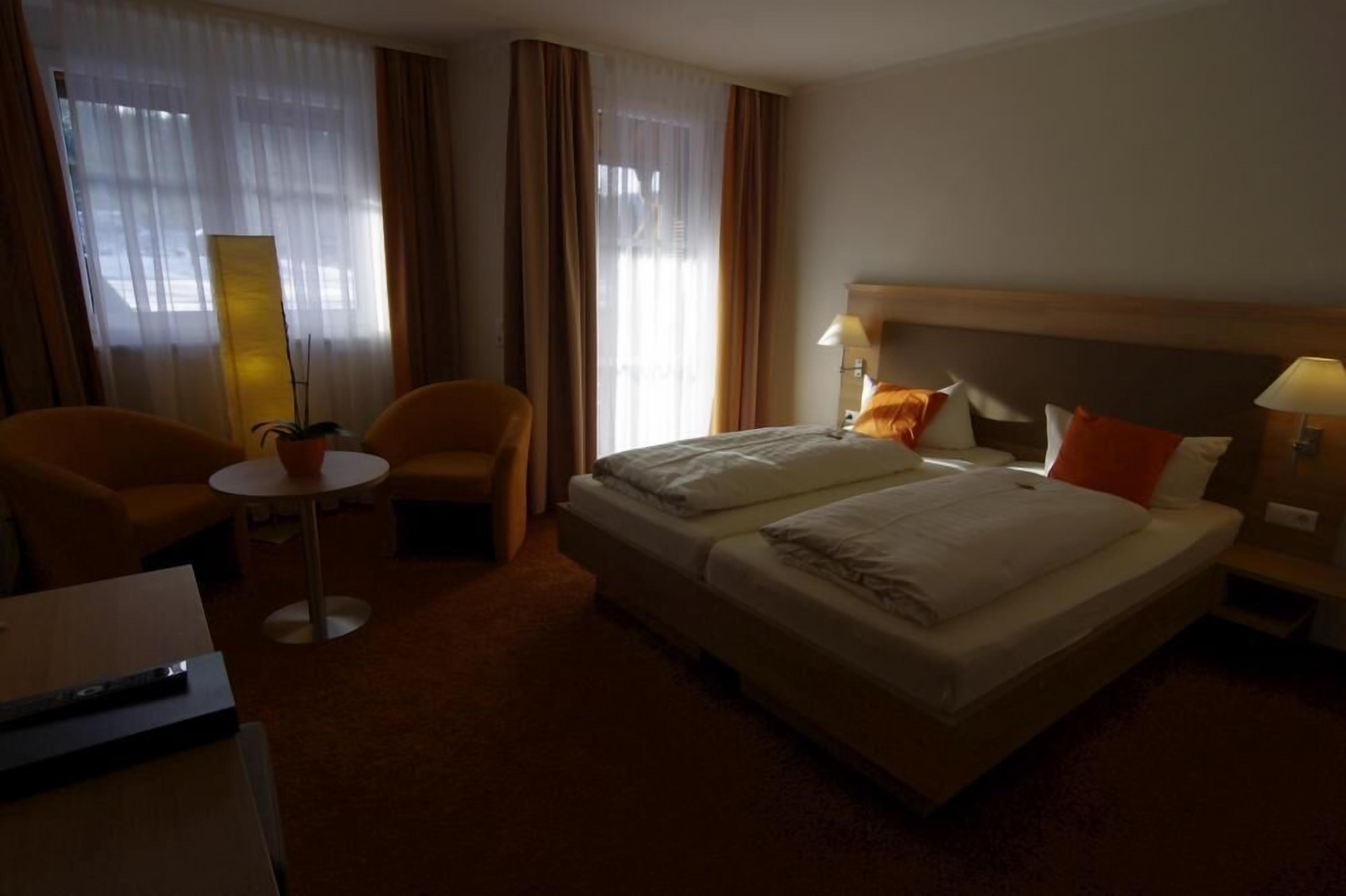 A hotel room with a double bed, two chairs, a small round table, a lamp, and a nightstand.