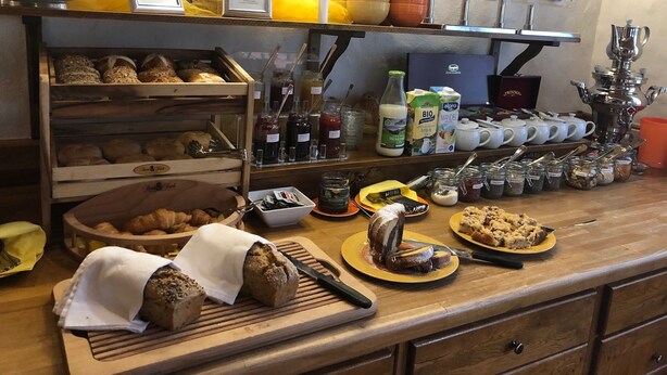 Un comptoir de boulangerie où sont exposés divers produits de boulangerie, des pots de confitures et une machine à café.