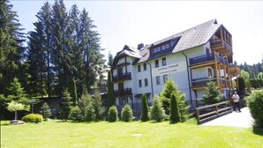 Un immeuble à plusieurs étages doté d’un balcon au dernier étage, entouré de verdure et d’arbres.