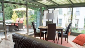 A covered outdoor seating area with a table and chairs, a sofa, and a view of the garden and buildings. - Pension Böttger (Wernigerode)