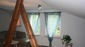 A cozy living room with a wooden beam, a sofa, a small table, and a potted plant. - Pension Böttger (Wernigerode)