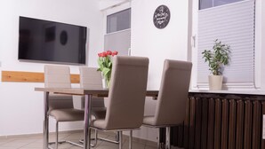 A modern dining area with a wooden table, four chairs, a flat-screen TV, a potted plant, and a sign on the wall. - Pension Böttger (Wernigerode)