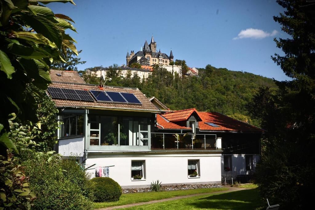 Ein Haus mit Solaranlage, Garten und Blick auf eine Burg auf einem Hügel.