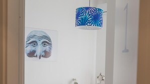 Une chambre à coucher comprenant un lit, un luminaire suspendu, une œuvre d’art accrochée au mur et une table de chevet avec une lampe.