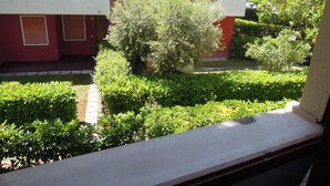 Ein rotes Gebäude mit Balkon, umgeben von gepflegter Bepflanzung und einem kleinen Wasserspiel.
