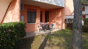 Ein Gebäude mit flachem Dach, einer überdachten Außenbereich-Sitzgelegenheit mit Tisch und Stühlen sowie einem kleinen Fenster.
