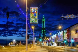 Een straat 's nachts met verlichte gebouwen, een opvallende toren en een kleurrijk glas-in-lood bord.