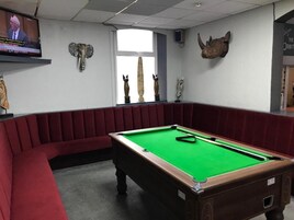Een biljartkamer met een pooltafel, rode gestoffeerde zittingen en decoratieve wandmontages.