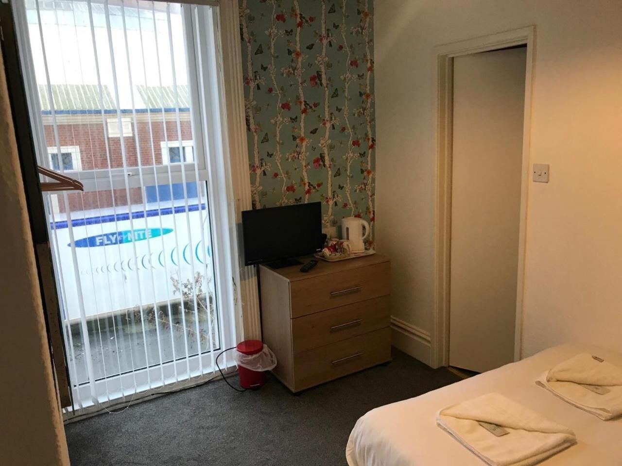 A hotel room with a bed, a dresser, a television, and a window with a view of a building.
