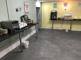 Een keukenhoek met een koffiezetapparaat, kopjes en een prullenbak.