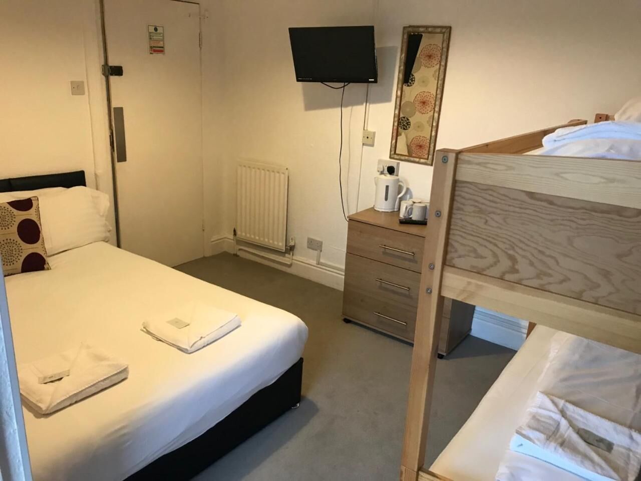 A hotel room with a bed, a dresser, a television, a radiator, and a mirror.