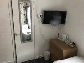 Hotelkamer met een bed, een houten dressoir, een aan de muur bevestigde televisie, een raam met gordijnen en een afvalbak.