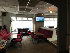 Een restaurant met rode banken en tafels, een televisie aan de muur en grote ramen met uitzicht.