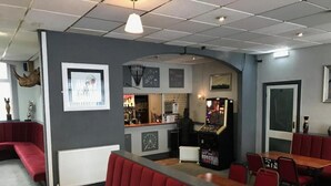 Restaurante com cabines vermelhas, mesas, área de bar e um balcão com diversos produtos.