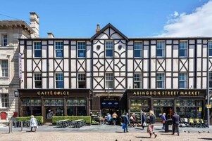 Een gebouw met borden 'CAFFÈ DOLCE' en 'ABINGDON STREET MARKET', met een traditionele architectuur, een symmetrische gevel en grote ramen.