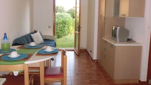 Un espacio habitable compacto con comedor, kitchenette y una puerta que da a un jardín.