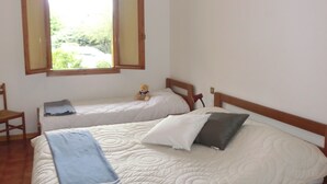 Un dormitorio con dos camas, una ventana, una silla y un osito de peluche sobre una de las camas.