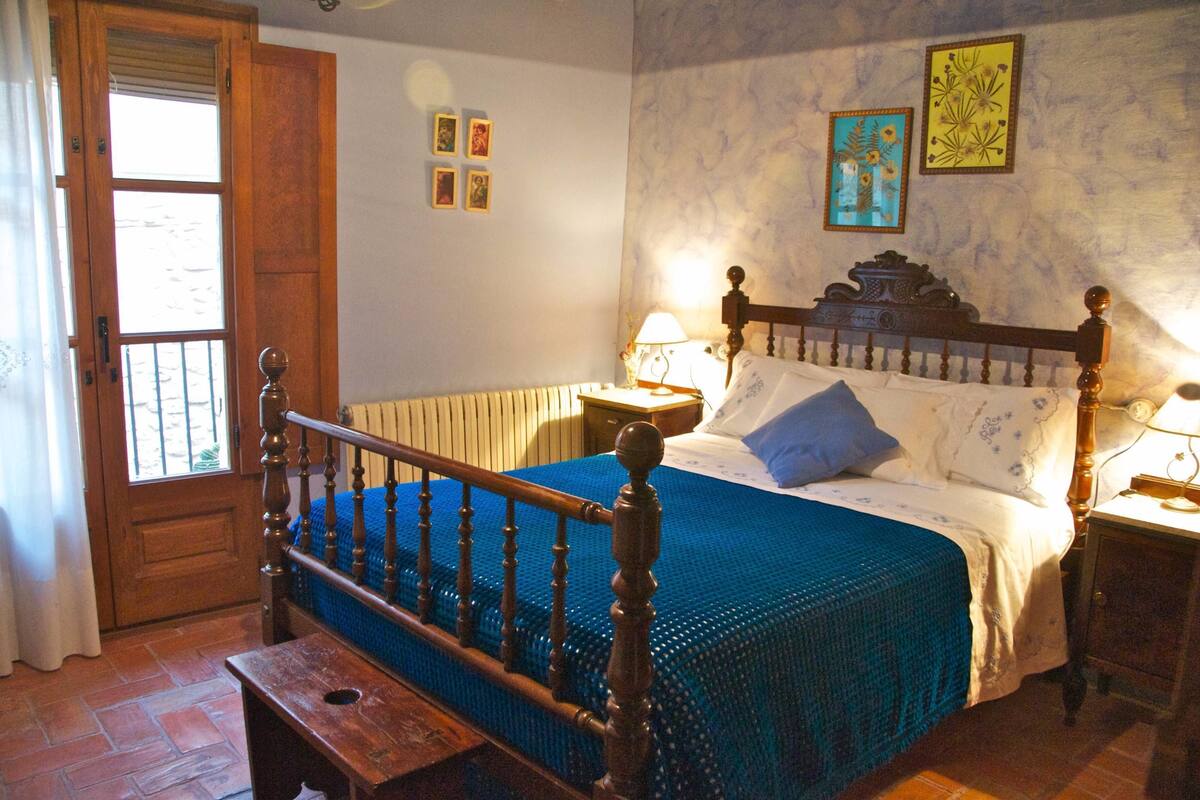 A bedroom with a wooden bed, a bench, a nightstand, and a door with a window.
