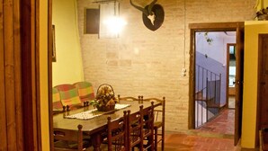 A dining area with a wooden table and chairs, a decorative wall hanging, and a view of a balcony through a door.