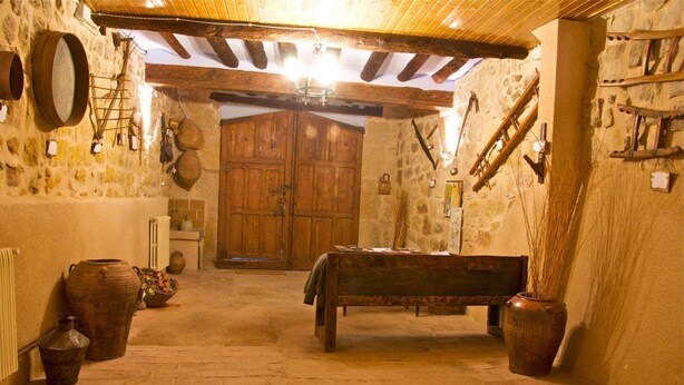 A rustic cellar with stone walls, wooden beams, and a central wooden bench.