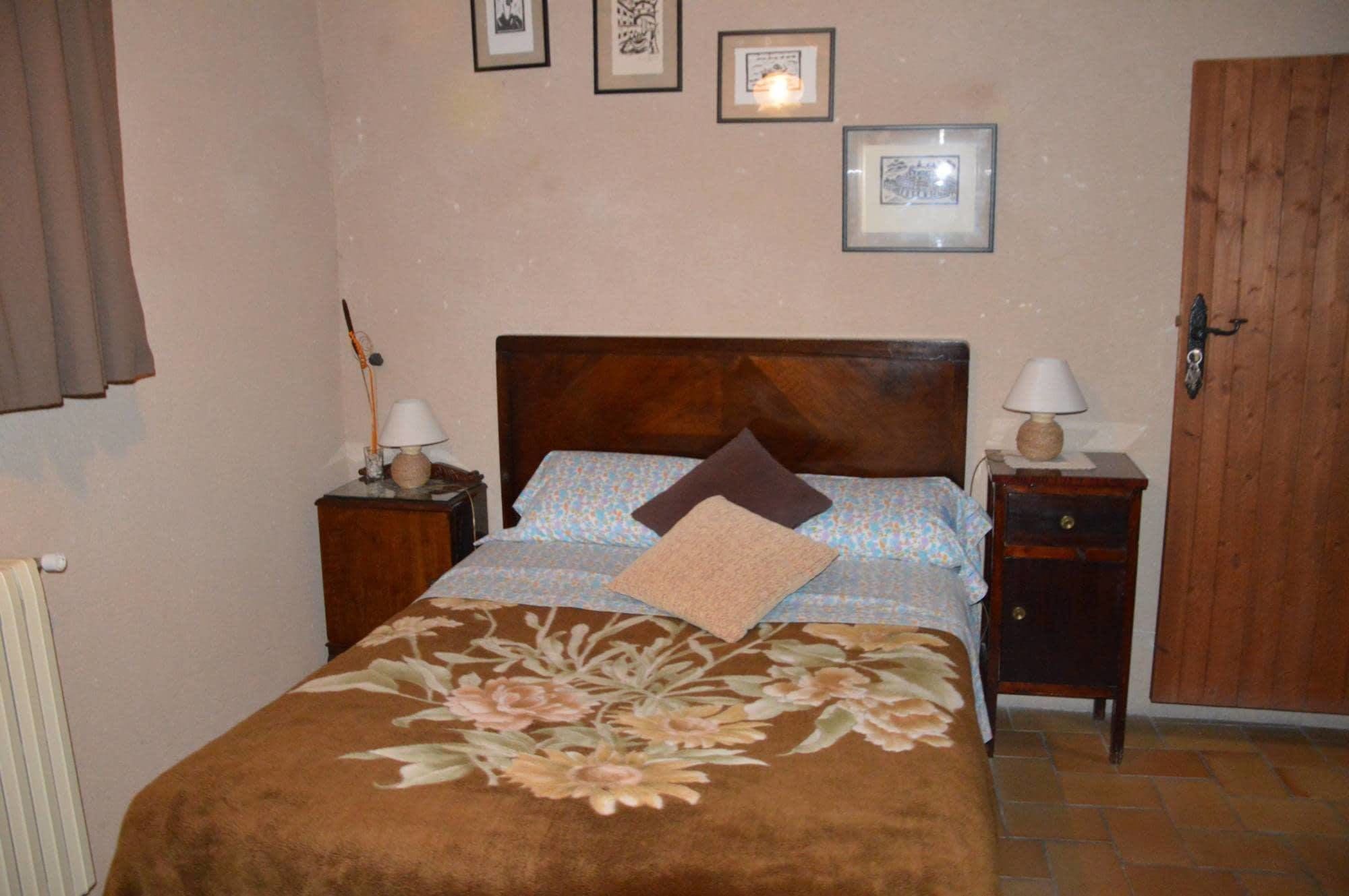 Un dormitorio con una cama de madera, dos mesitas de noche con lámparas, una puerta y tres cuadros enmarcados en la pared.