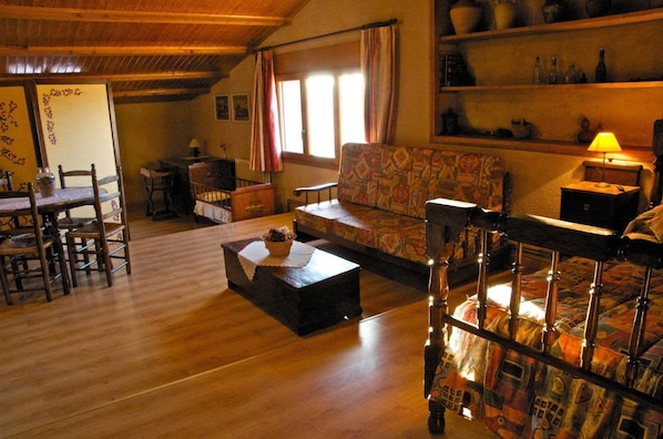 Una sala de estar acogedora con muebles de madera, un sofá estampado, una mesa de comedor con sillas y una cuna para bebé.