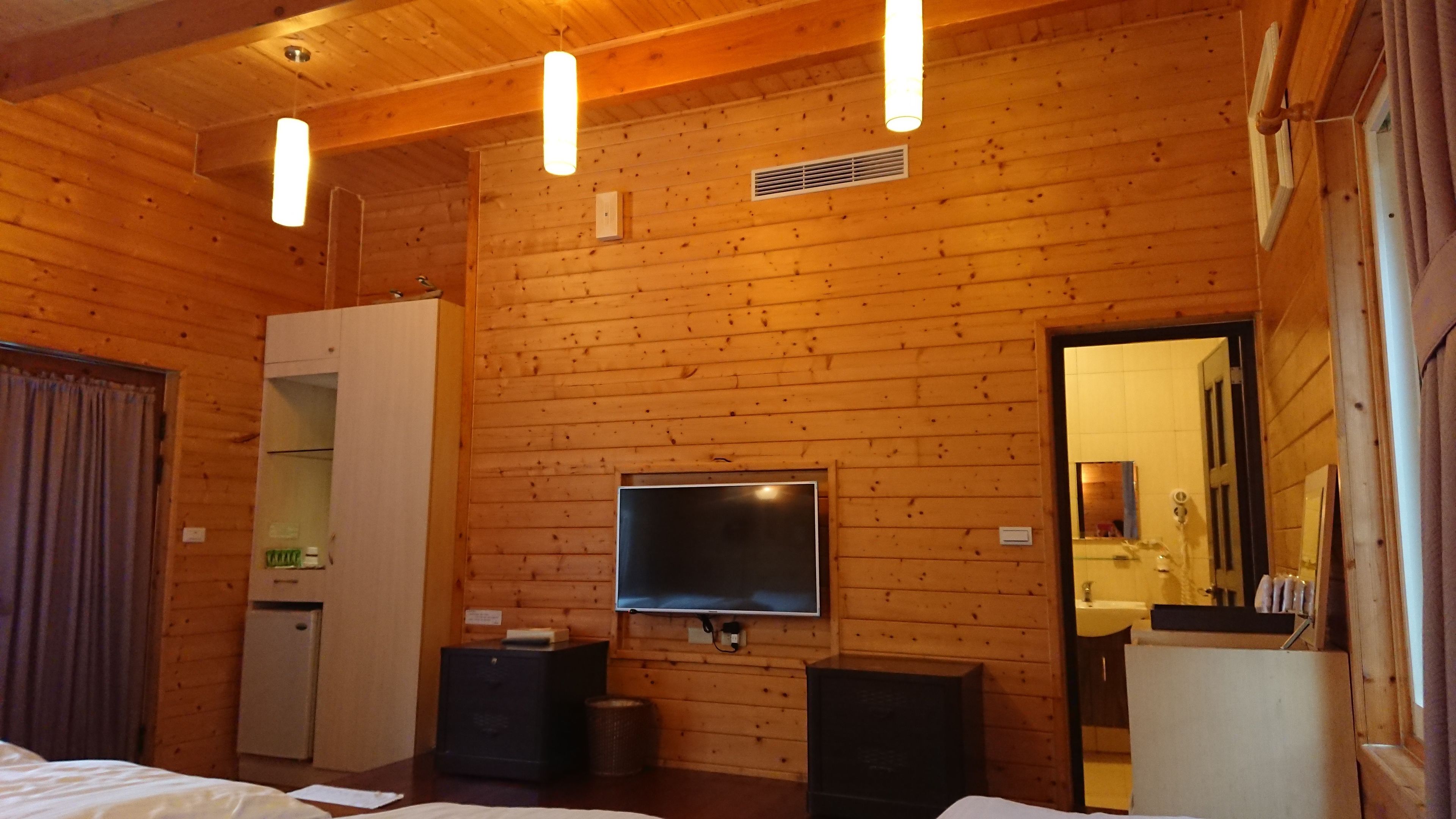 A wooden-paneled room with a bed, a television, a small refrigerator, and a bathroom visible through an open door.