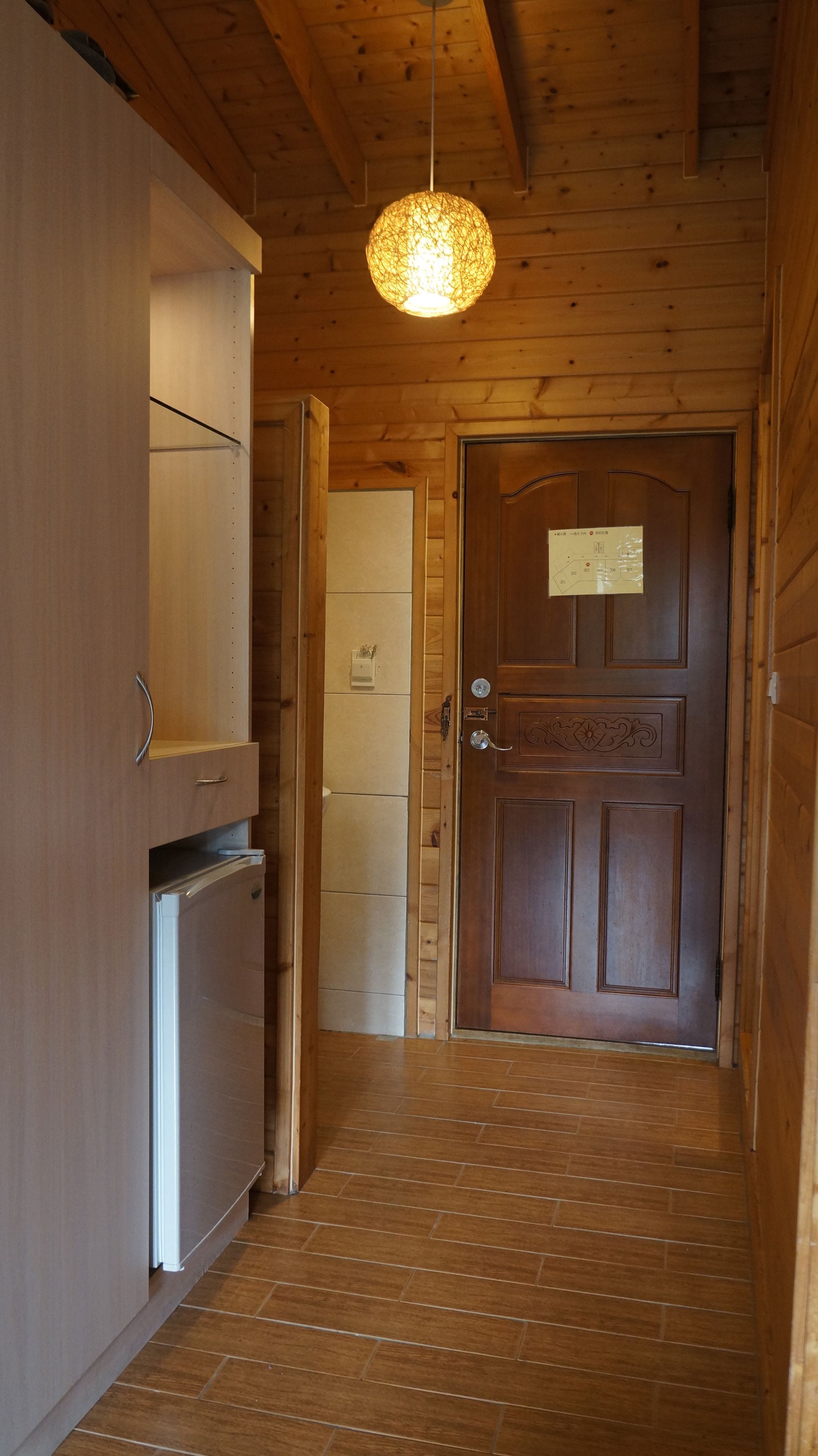 A wooden interior with a door, a hanging light fixture, and a refrigerator.