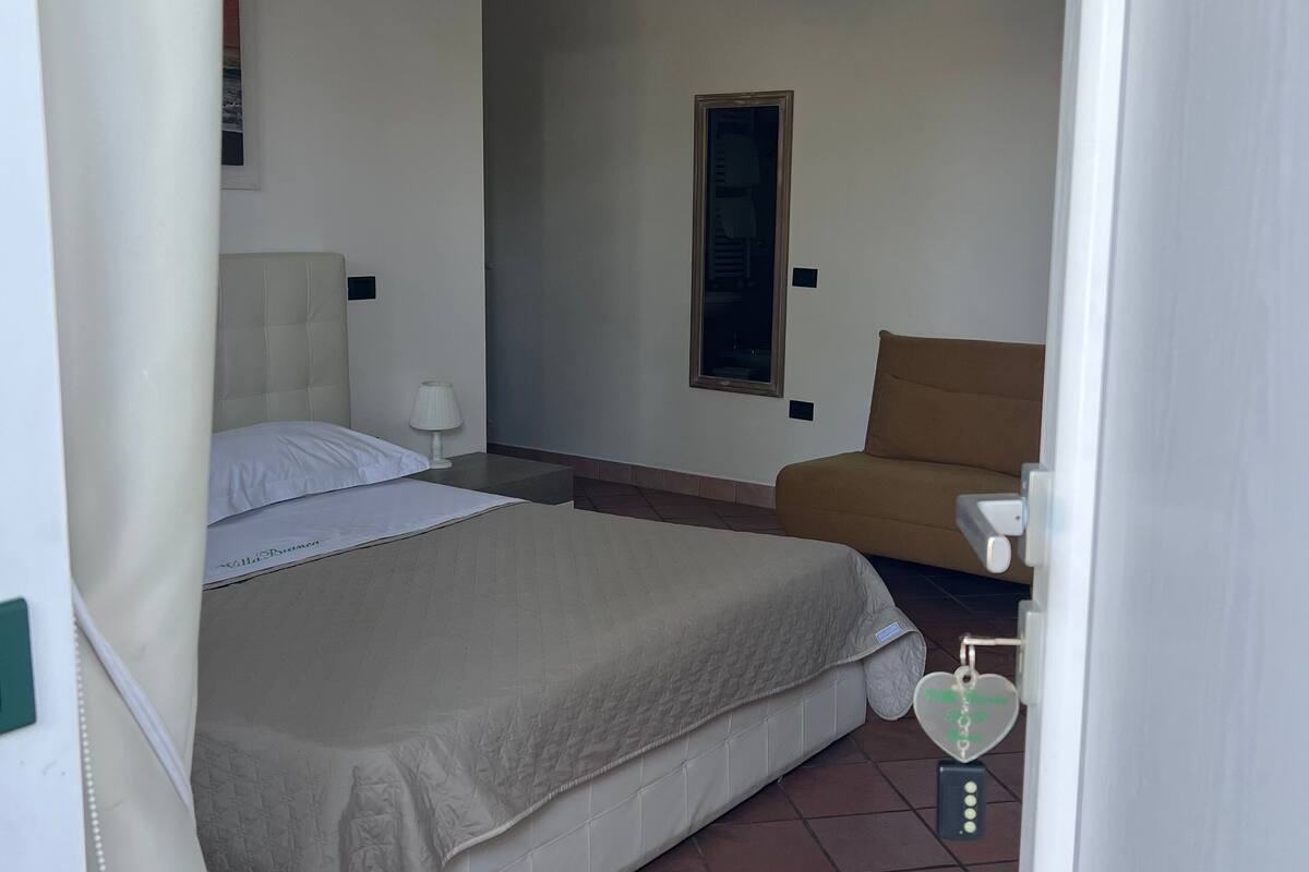 Ein Schlafzimmer mit Bett, Sessel, Nachttisch, Pendelleuchte und einer Tür mit herzförmigem Schloss.