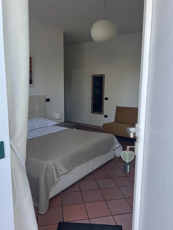 A bedroom with a bed, a chair, a bedside table, a hanging light fixture, and a door with a heart-shaped lock. - Villa Bianca (Castellammare di Stabia)