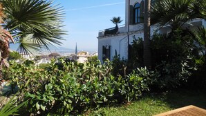 A garden with lush greenery, a wooden bench, and a white building with arched windows. - Villa Bianca (Castellammare di Stabia)
