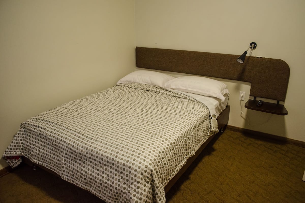 Una cama individual con una colcha estampada, un cabecero y una mesita de noche con una lámpara.
