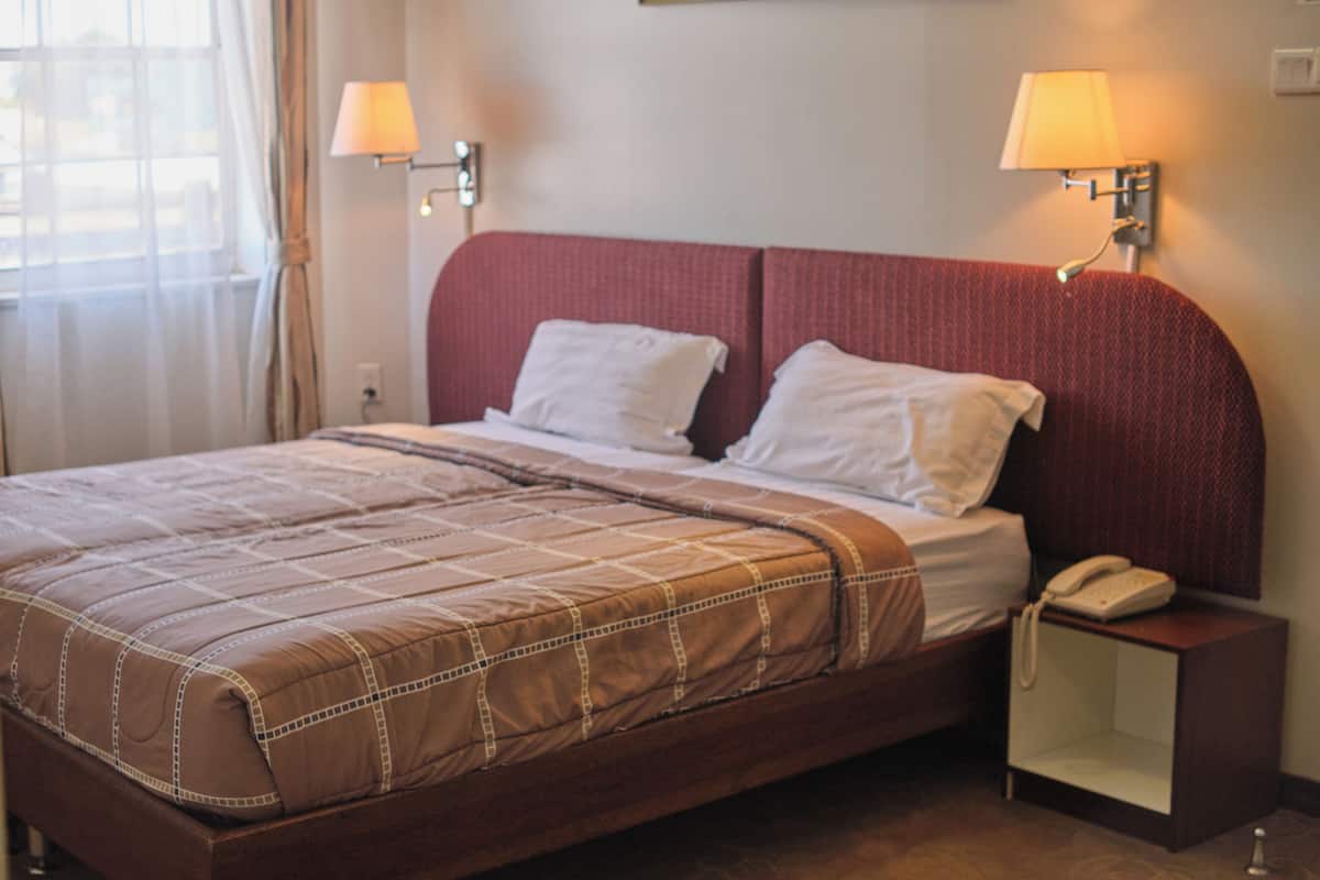 Habitación de hotel con cama, dos lámparas de noche, una mesita de noche con teléfono y ventana con cortinas.
