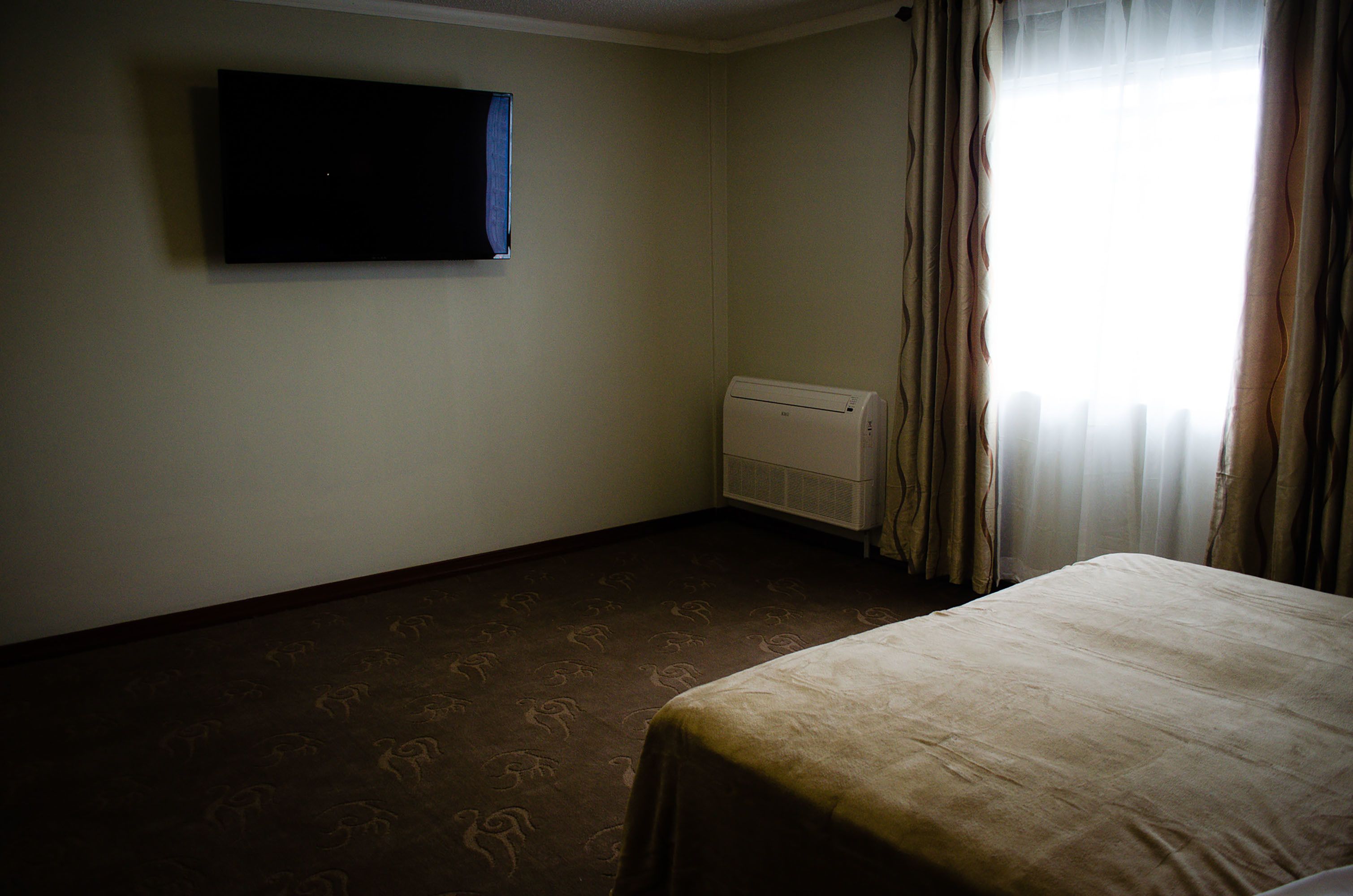 Habitación de hotel con cama, televisor de pantalla plana montado en la pared, aire acondicionado y ventana con cortinas.