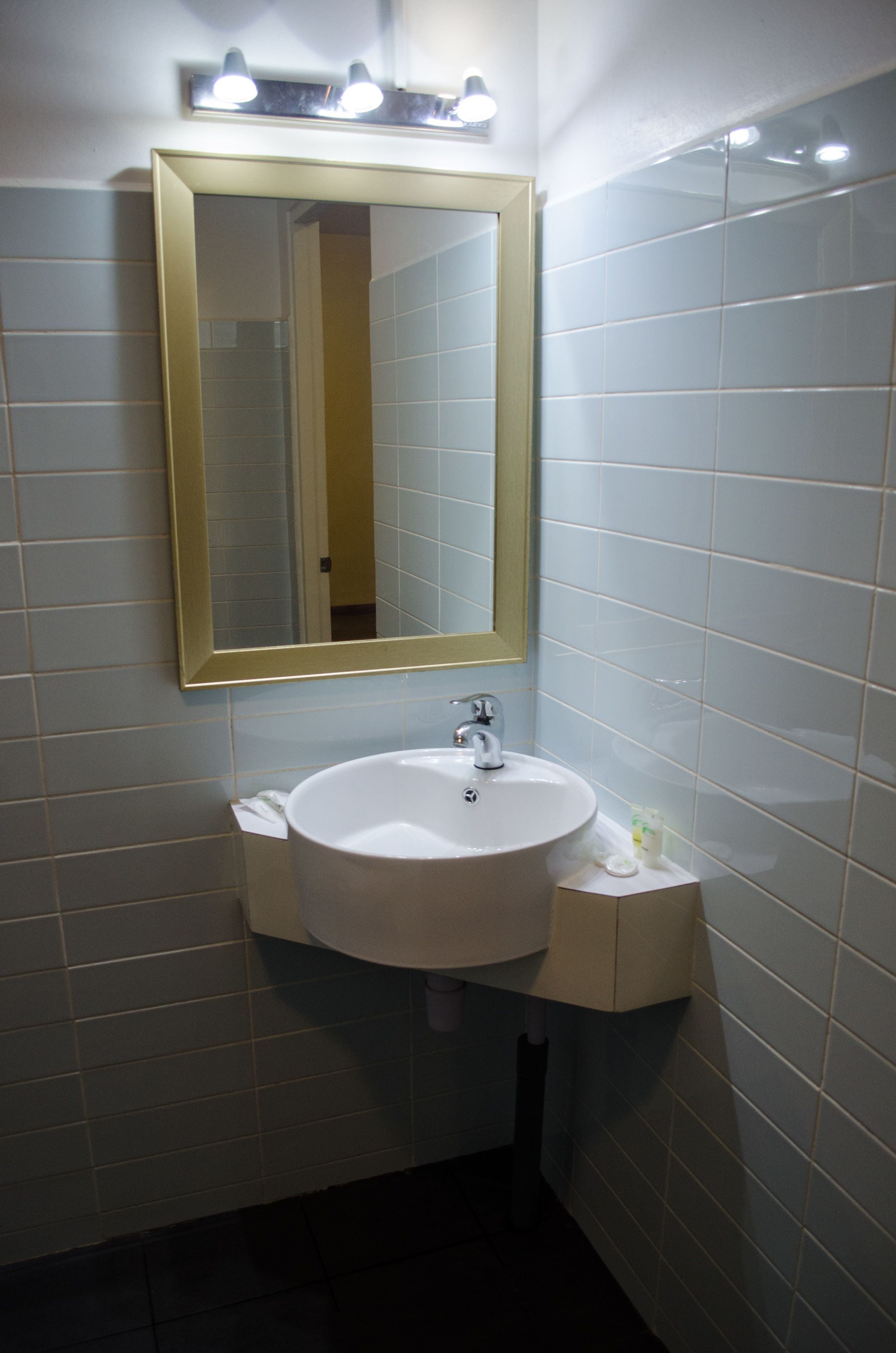 Un baño con un lavamanos blanco, un espejo con marco dorado y baldosas de colores claros.