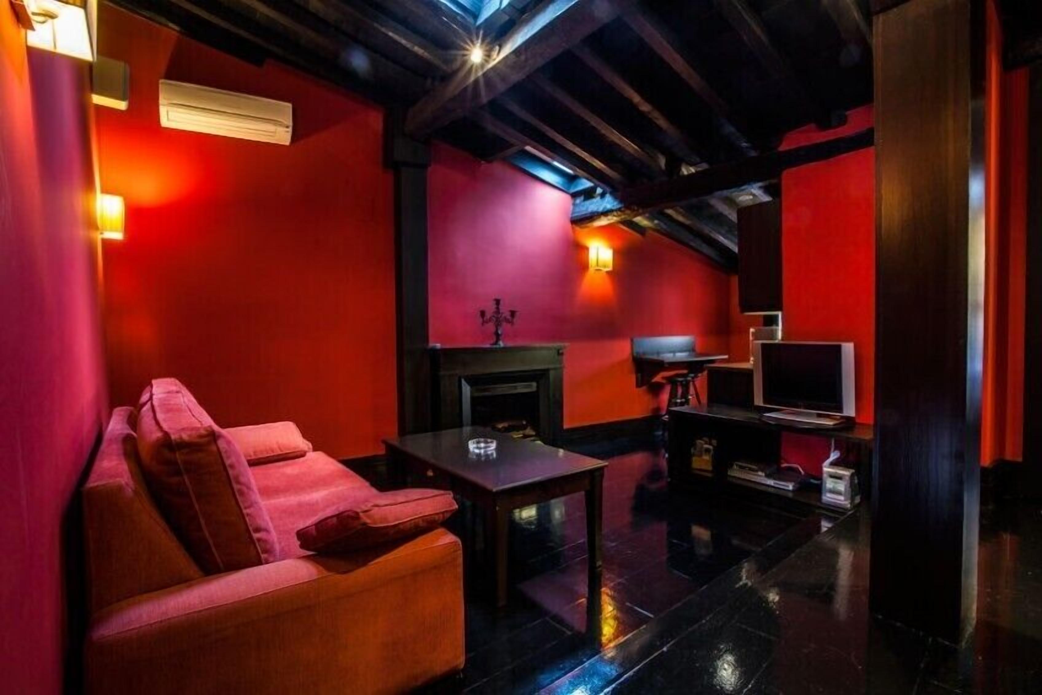 Una habitación tenuemente iluminada con paredes rojas, un sofá de cuero, una mesita, una chimenea y un televisor.