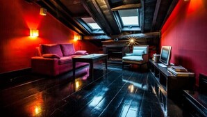 Une pièce mansardée chaleureuse avec un mur rouge, un canapé, un fauteuil, une petite table et un téléviseur.