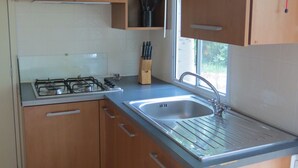 Una cocina compacta con armarios de madera, estufa a gas y pileta de acero inoxidable.