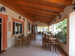 A covered outdoor dining area with wooden tables and chairs, a tiled floor, and a view of greenery outside. - Camping Bella Vista (Albenga)