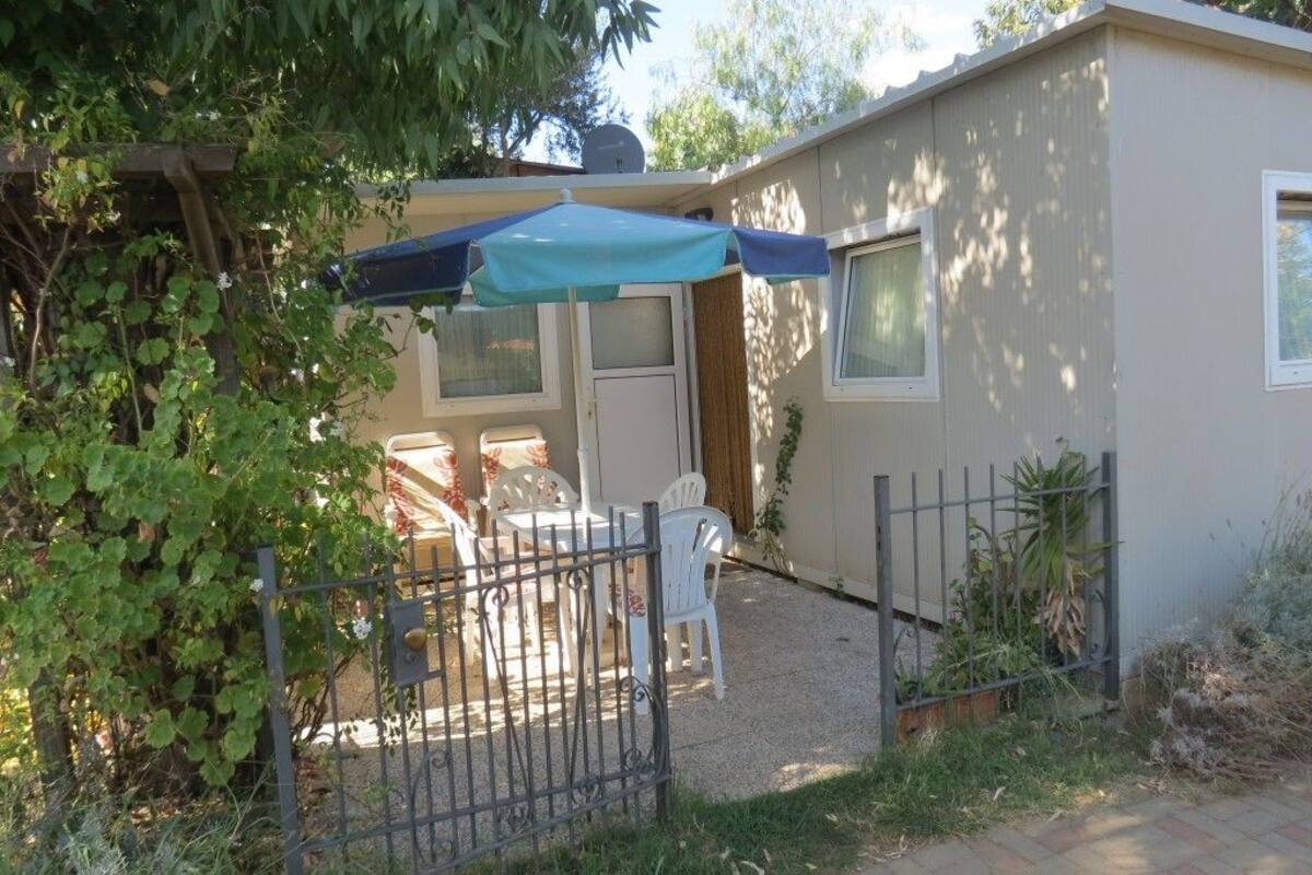 Une petite maison de plain-pied dotée d’un patio comprenant une table et des chaises, un espace salon couvert et un jardin clôturé.