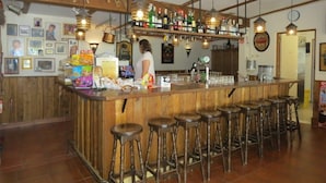 Zona de bar con taburetes de madera, barra y diferentes botellas y vasos.