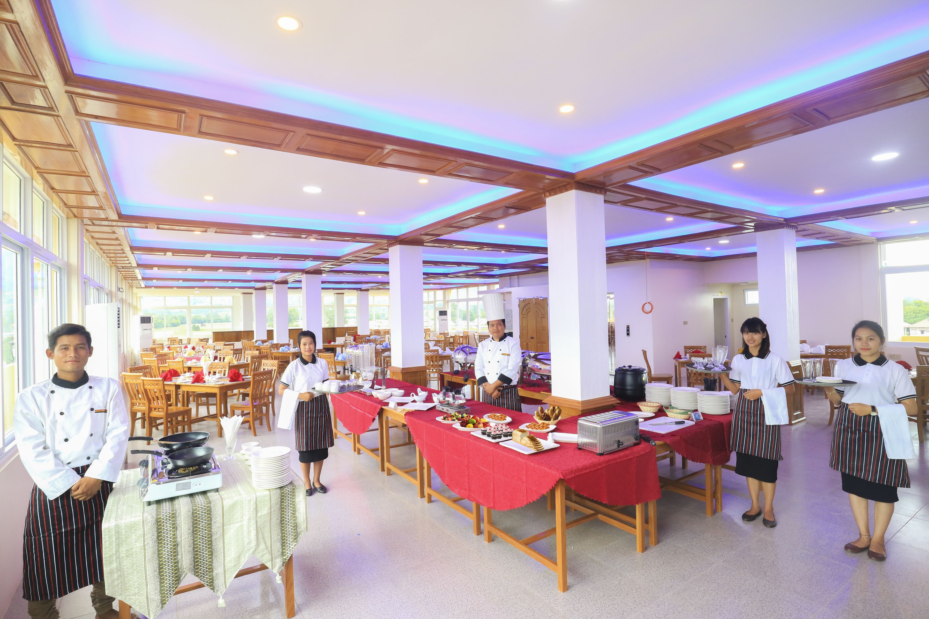 Une salle à manger spacieuse, dotée de nombreuses tables, de chaises et où une grande variété de plats sont présentés.