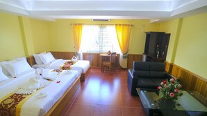 A hotel room with two beds, a sofa, a small table with a vase of flowers, and a window with curtains.
