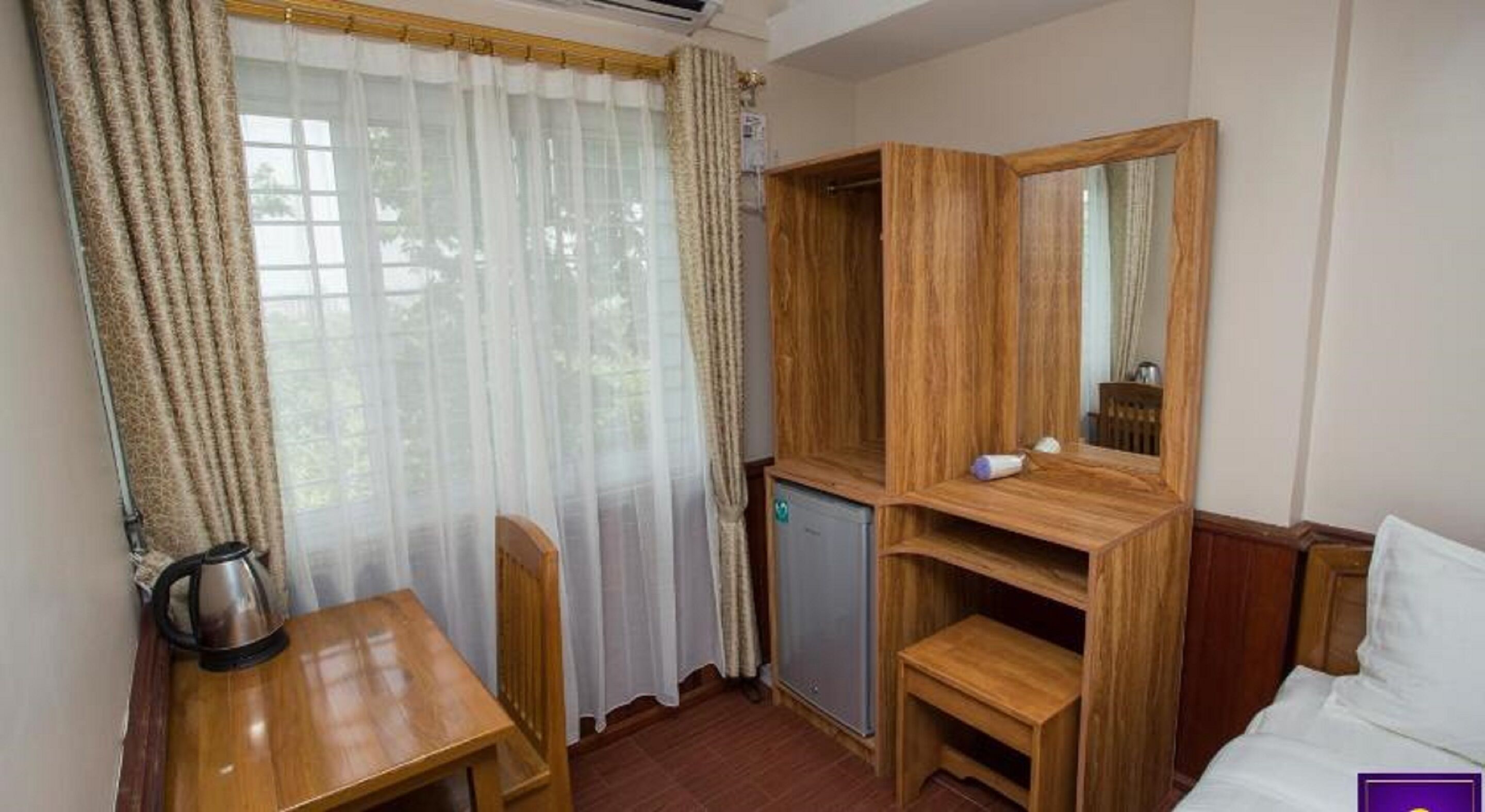A compact hotel room with a wooden desk, a small cabinet, a mirror, and a bed.