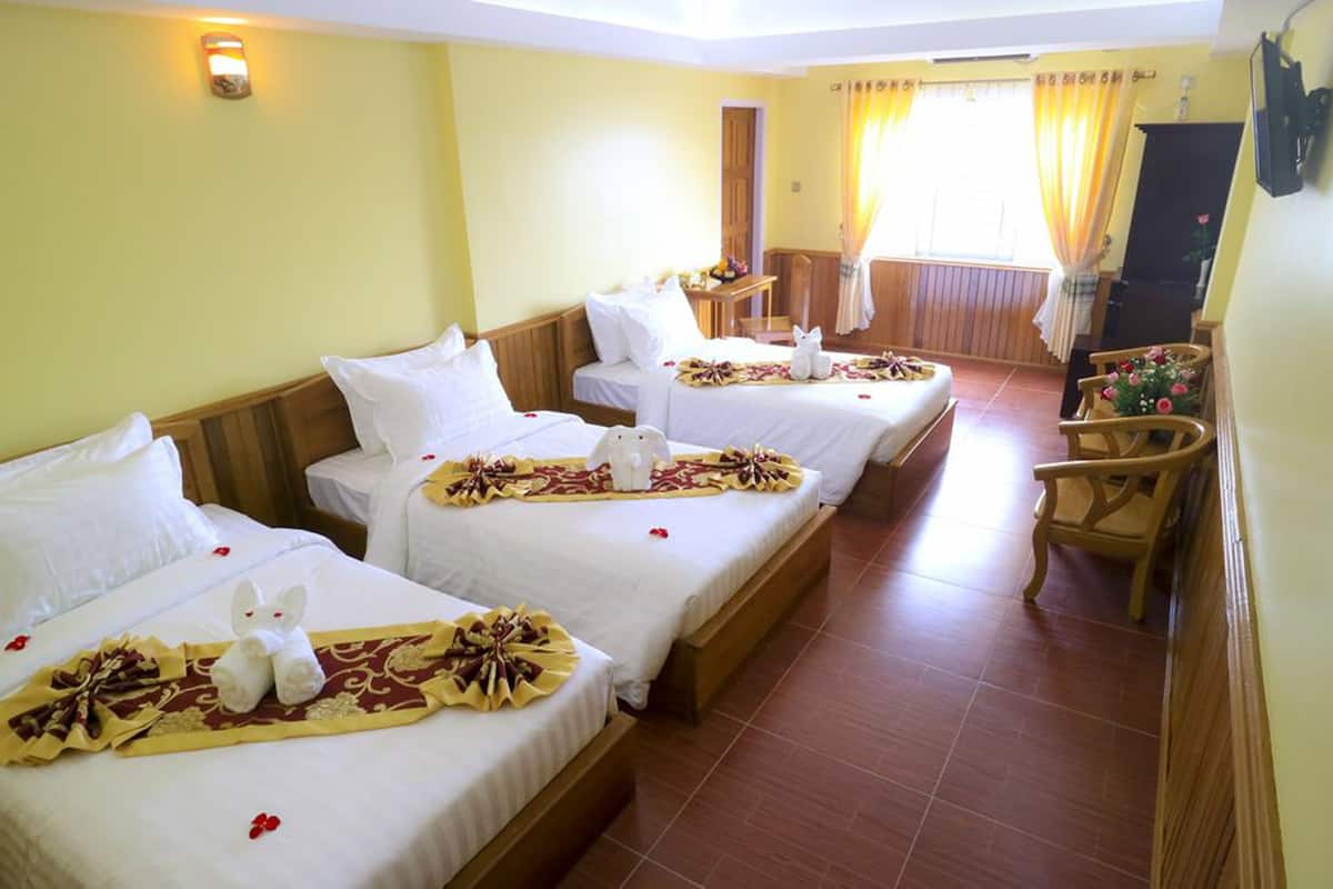 Une chambre d’hôtel avec trois lits, chacun agrémenté de draps blancs et de compositions florales décoratives. On y trouve une chaise en bois et une petite table sur laquelle est posé un vase de fleurs.