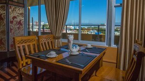 A dining area with a table set for two, large windows with curtains, and a view of a cityscape.